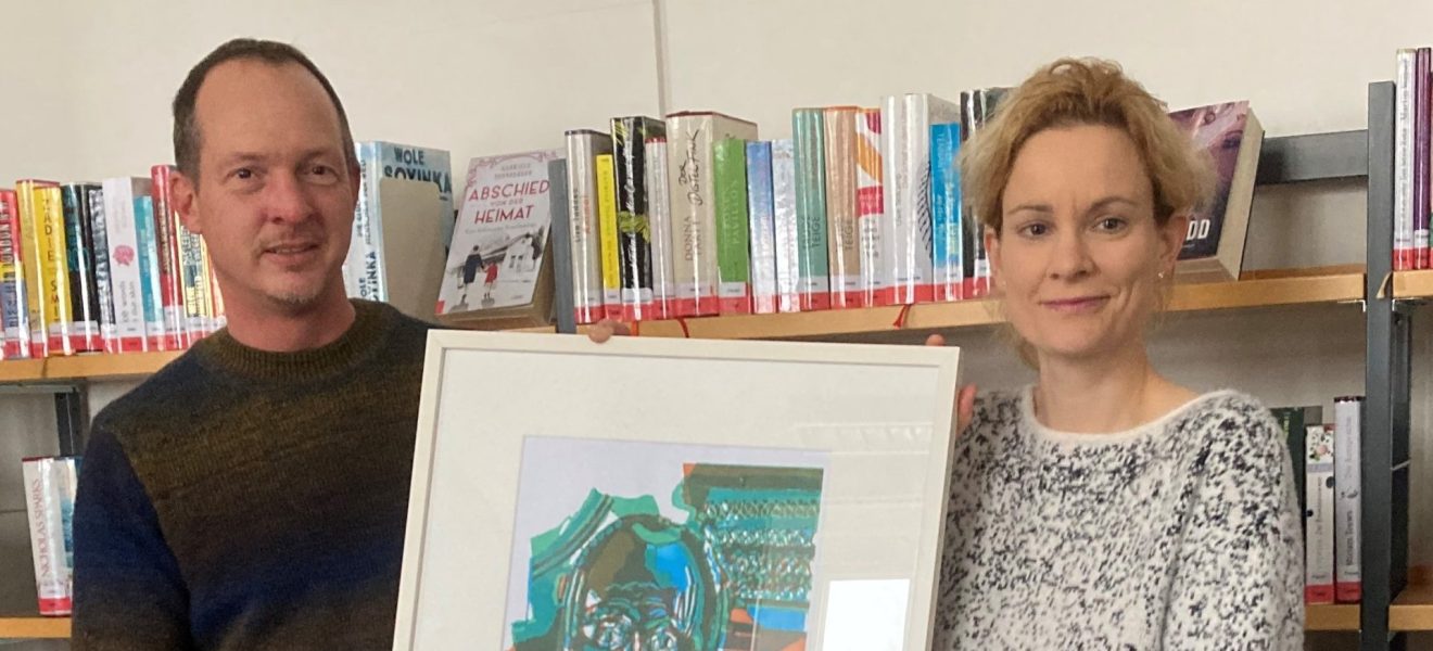 Sonja Hohnholt, Leiterin der Stadtbibliothek Aurich, und Welf-Gerrit Otto, Leiter der Kulturagentur der Ostfriesischen Landschaft, präsentieren das erste Bild der Wechselausstellung (Foto: Stadtbibliothek Aurich)